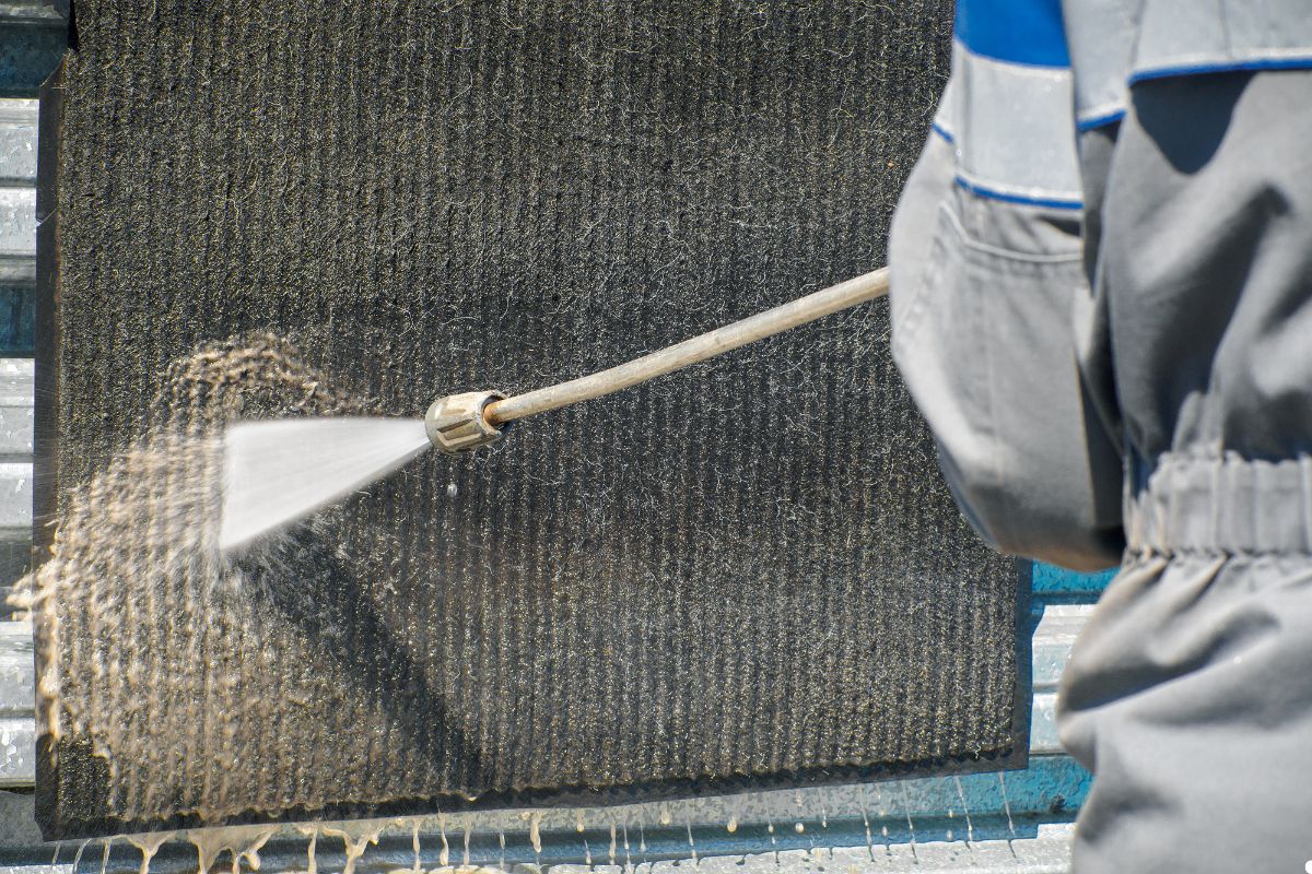 A man uses a hose to clean a wall, spraying water to remove dirt and grime from the surface.