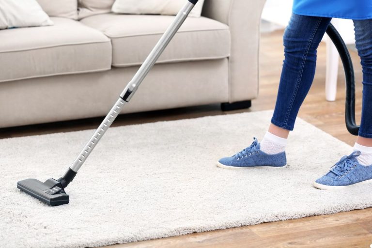 A woman vacuuming a rug with a vacuum cleaner, demonstrating household cleaning in a tidy living space.